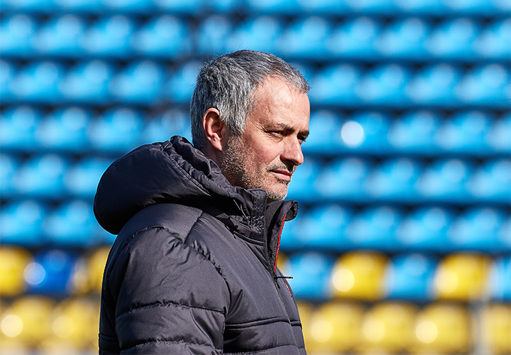 The Manchester United manager, Jose Mourinho, is sporting a winter adidas jacket and a serious / focused look on his face.  The stands are empty.  Training.