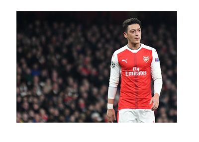 Mesut Ozil wearing the Arsenal home kit.  A little confused on the pitch.  Walking.