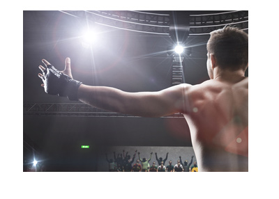 Victorious mixed martial artist celebrating with his hands up and to the side. Public in attendance cheering.