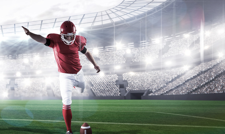 The NFL player is kicking the ball during the goal kick in the game in front of a full stadium. Featured article is focused on football betting tips.