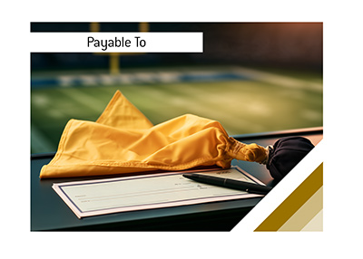 Yellow football penalty flag beside an unfinished cheque and black pen, with a football field blurred in the background.