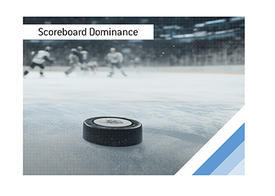 Hockey puck in sharp focus on ice with blurred players in background.