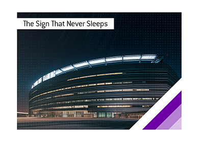 Illuminated naming-rights sign glowing above a modern football stadium at night.
