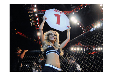 Ring side girl at a UFC event holding the Round 1 sign. The lights are on. Fight time.